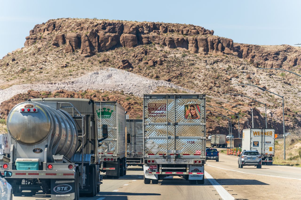 Vibrant Indian and American trucks travel on an Arizona highway with desert scenery.