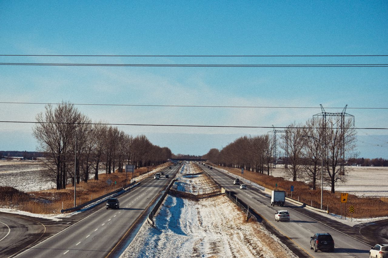 A scenic view of a highway in winter, with cars and trucks under a clear blue sky.